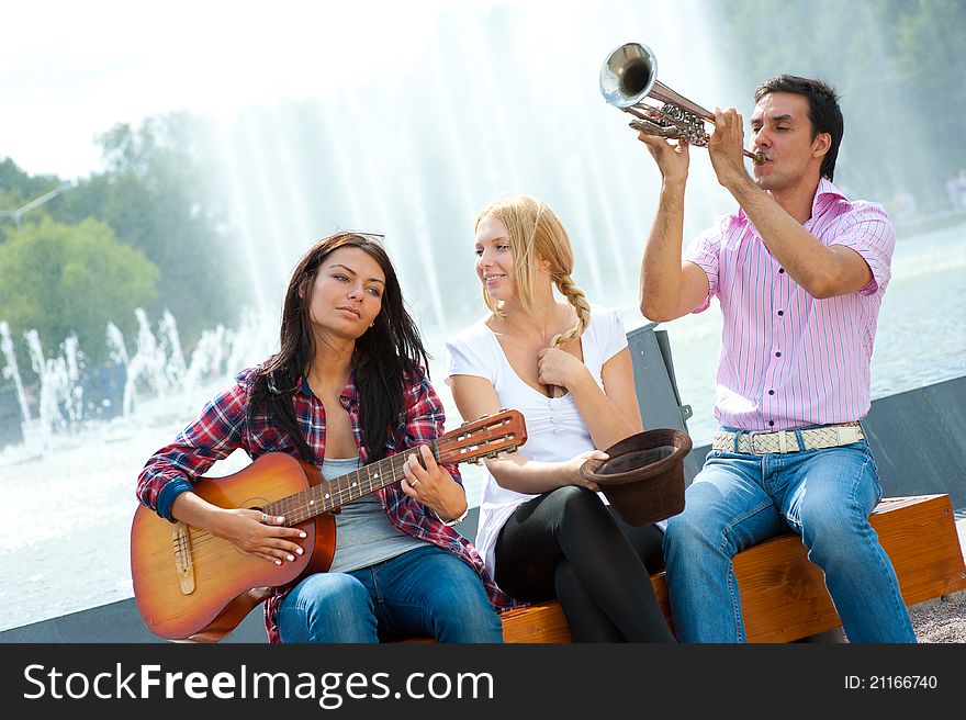Young friends play the guitar and trumpet in the park