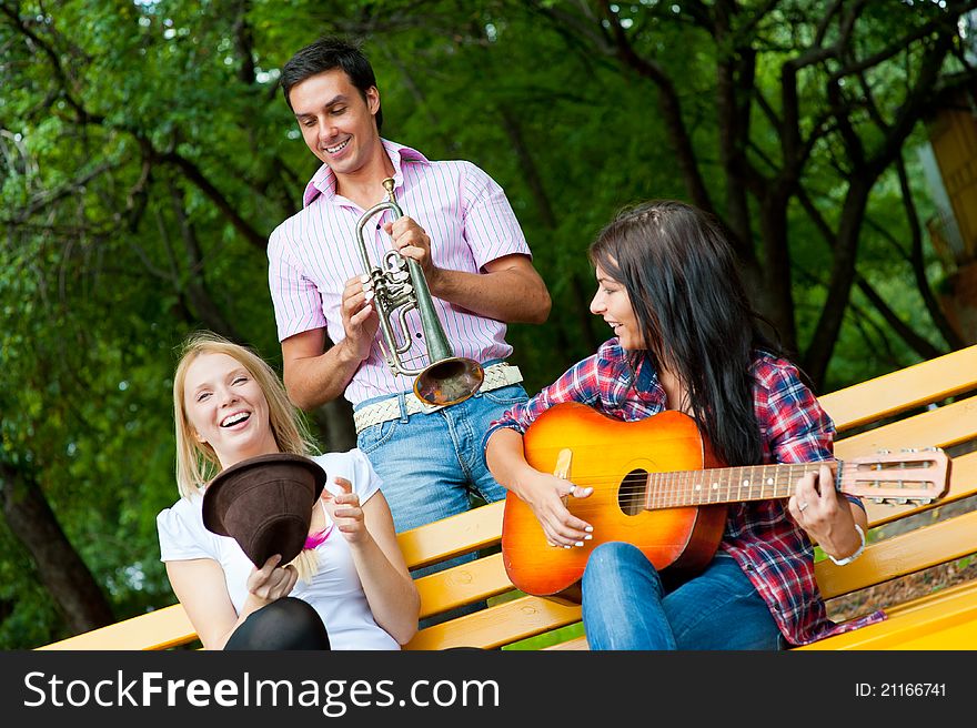 Young friends play the guitar and trumpet in the park