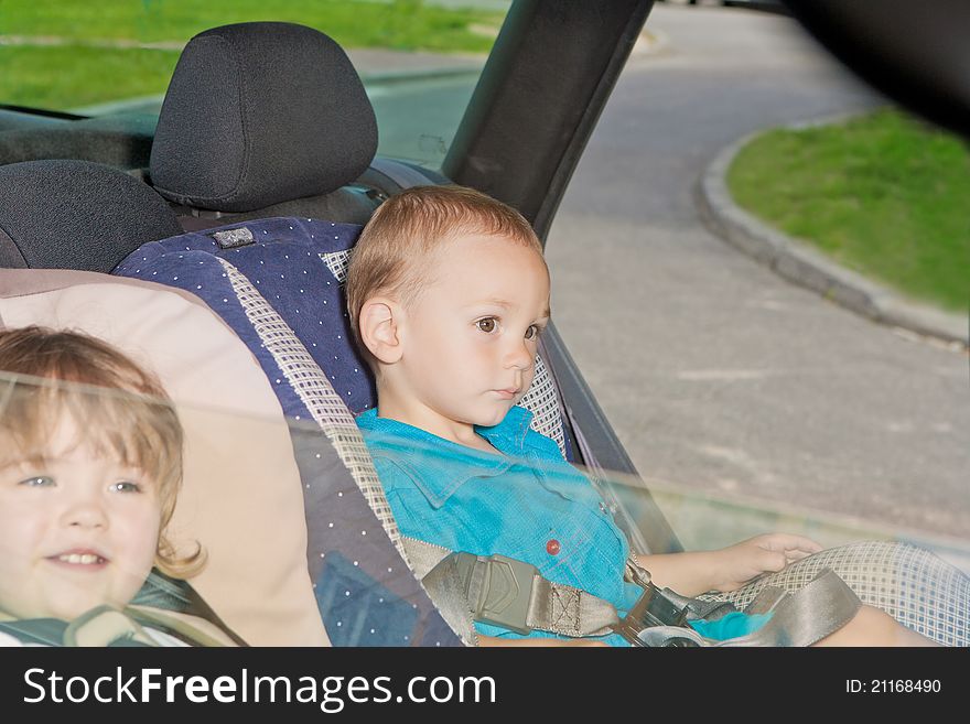 Two little kids sitting on back seat in child safety seats looking on windows. Two little kids sitting on back seat in child safety seats looking on windows