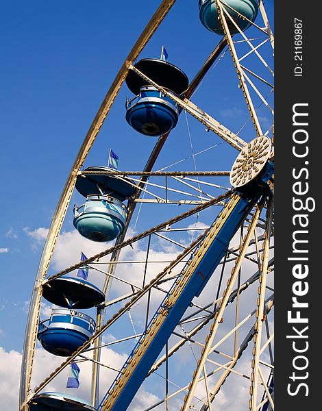 A view of the colorful light and dark blue cars of a ferris wheel backed by a bright blue sky and white clouds at the Cabarrus County Fair. A view of the colorful light and dark blue cars of a ferris wheel backed by a bright blue sky and white clouds at the Cabarrus County Fair.