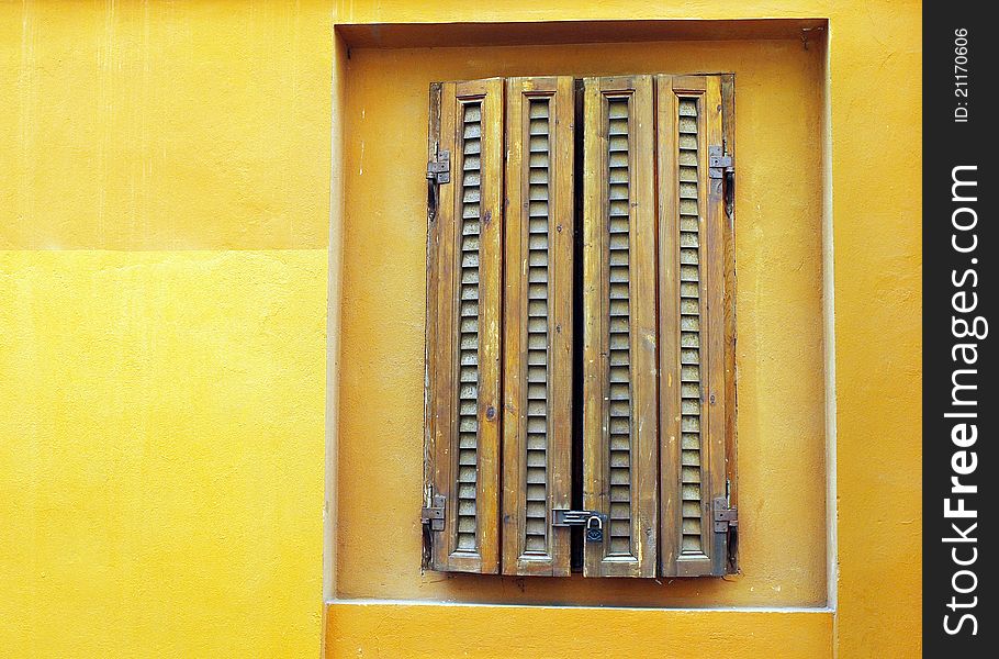 A background with a view of a closed window on an old yellow wall.
