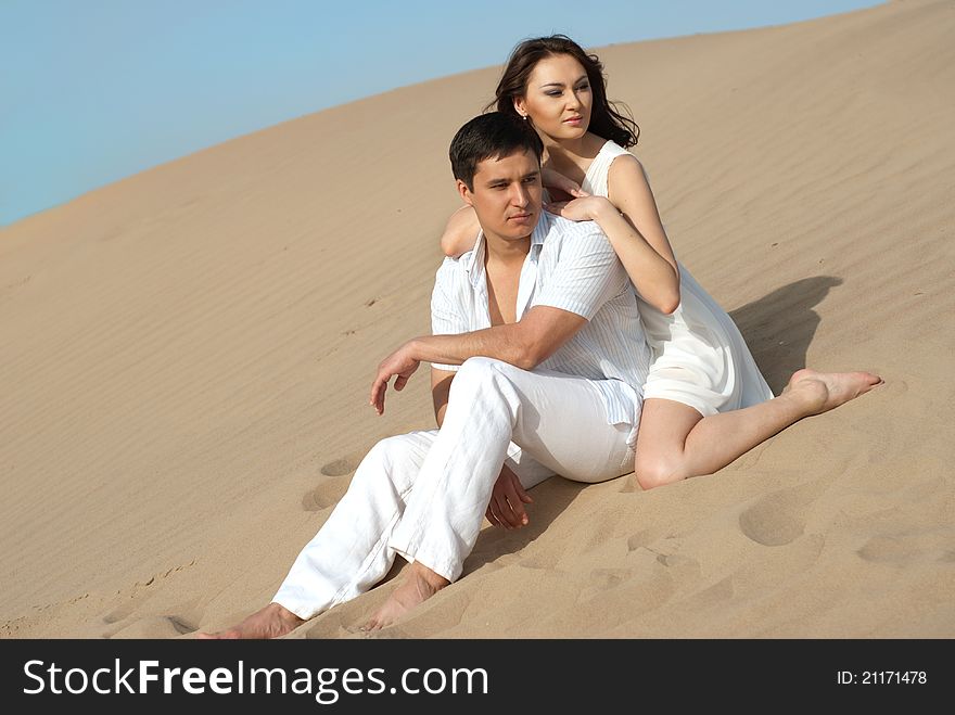 Young couple in love in a white dress sitting on sand. Young couple in love in a white dress sitting on sand
