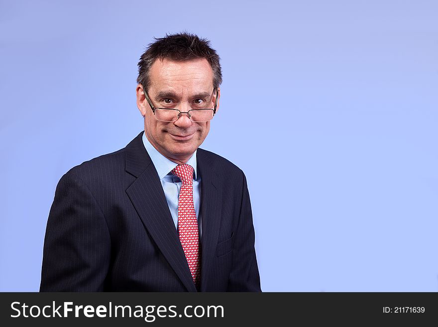 Smiling Business Man in Suit with Cheesy Expression Looking Over Glasses on Blue Background. Smiling Business Man in Suit with Cheesy Expression Looking Over Glasses on Blue Background