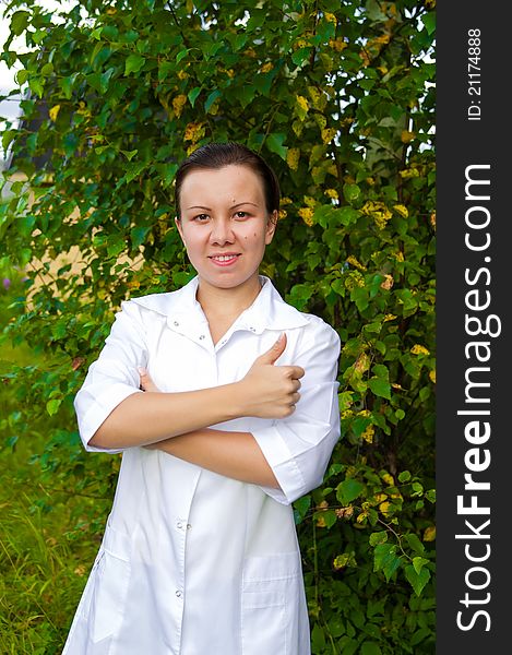 Cheerful smiling woman doctor outdoors in the garden with arms across