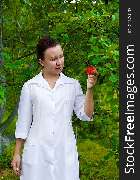 A pretty woman doctor handing an apple in the apple garden. A pretty woman doctor handing an apple in the apple garden