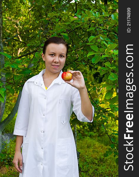 A pretty woman doctor handing an apple in the apple garden. A pretty woman doctor handing an apple in the apple garden