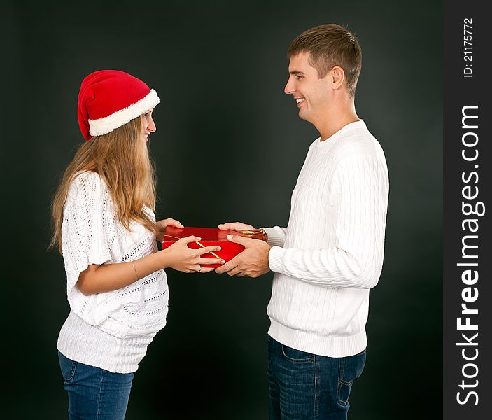 The men gives the gift pregnant girl in Santa hat in studio on dark background. The men gives the gift pregnant girl in Santa hat in studio on dark background