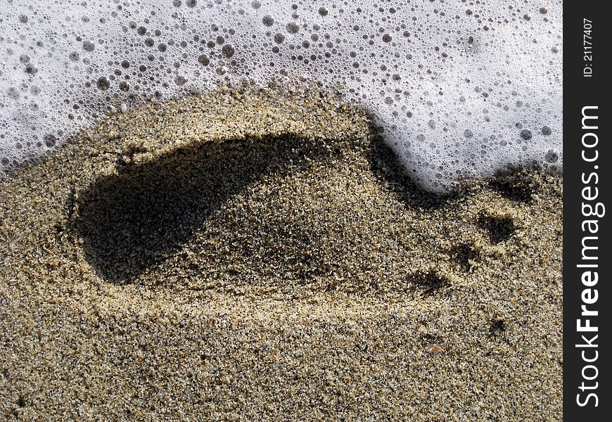 Sea foam washing away foot print in the sand. Sea foam washing away foot print in the sand