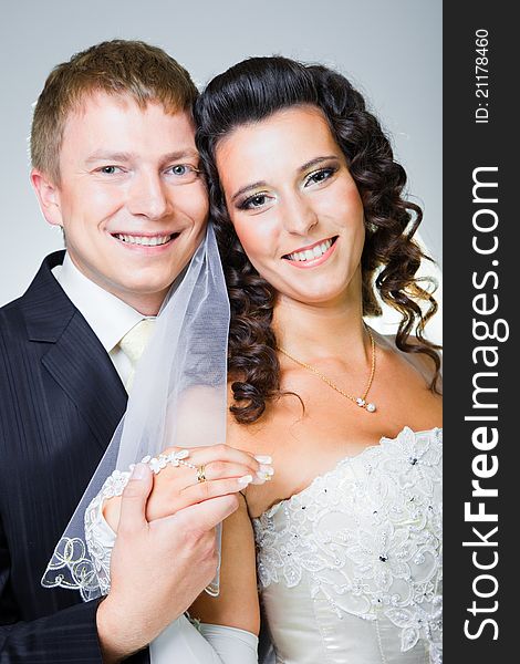 Studio portrait of young elegant enamored just married bride and groom and embracing on grey background
