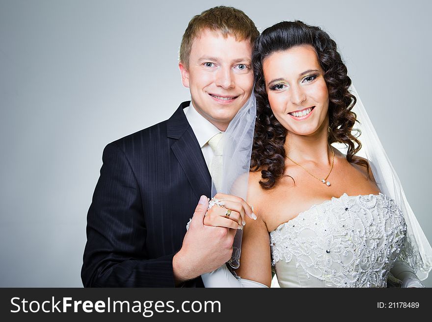 Studio portrait of young elegant enamored just married bride and groom and embracing on grey background