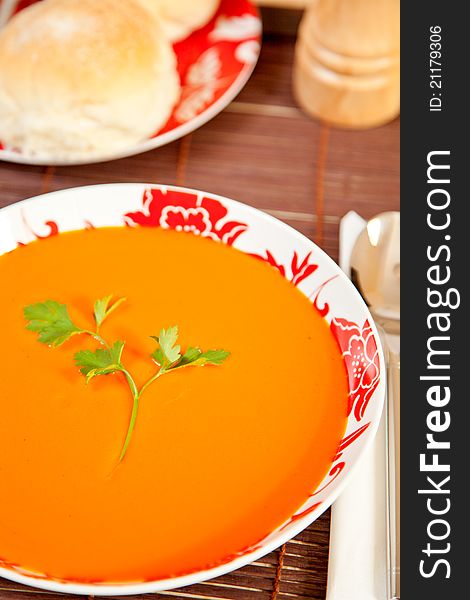 A bowl of tomato soup with bread in the background.