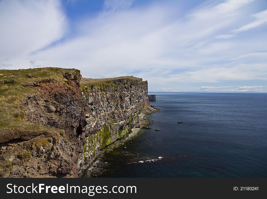 The sea cliffs at Látrabjarg in the westfjords with the mountains at Snæfellsnes in the distance.