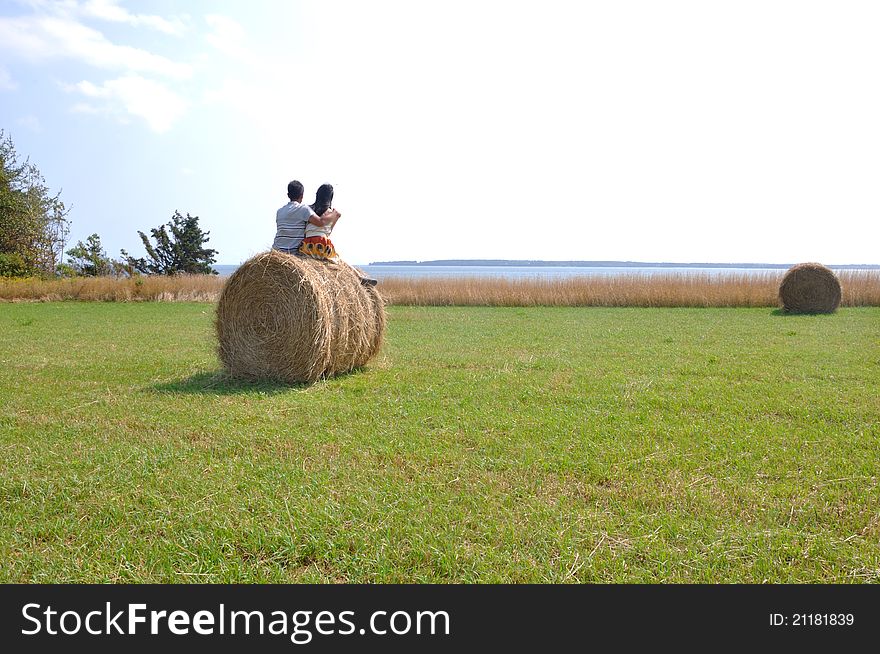 A lovely couple are sitting on a straw roll on summer farmer field in Price Edward Island, Canada, watching the ocean of Atlantic. A lovely couple are sitting on a straw roll on summer farmer field in Price Edward Island, Canada, watching the ocean of Atlantic.