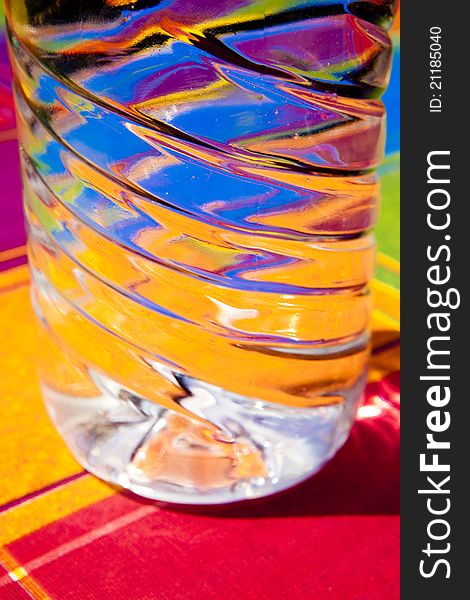 Water reflection of colors within a transparent plastic bottle on a table with tablecloth colors. Water reflection of colors within a transparent plastic bottle on a table with tablecloth colors