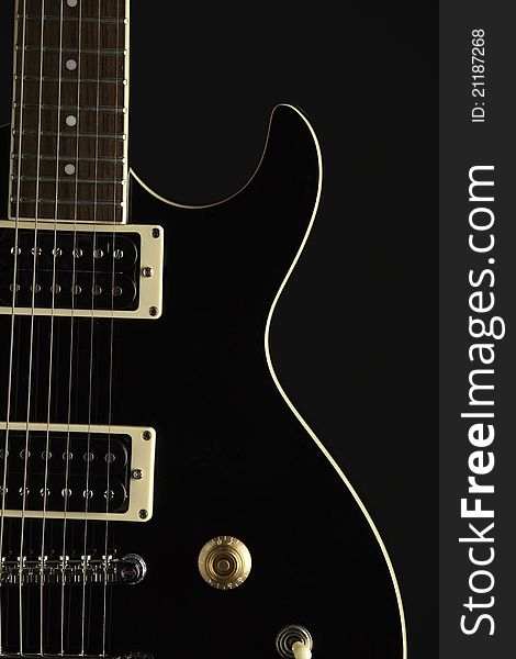 A black electric guitar isolated against a black background. A black electric guitar isolated against a black background