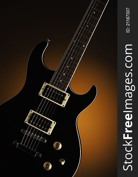 A black electric guitar isolated against a spotlight orange background. A black electric guitar isolated against a spotlight orange background