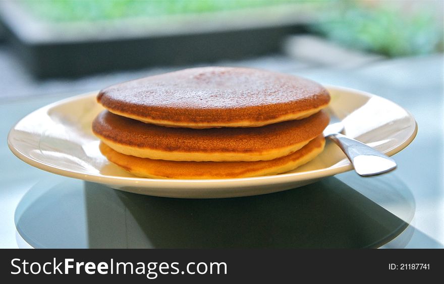 Stack of 3 pancakes on a plate with a garden in the background. Stack of 3 pancakes on a plate with a garden in the background