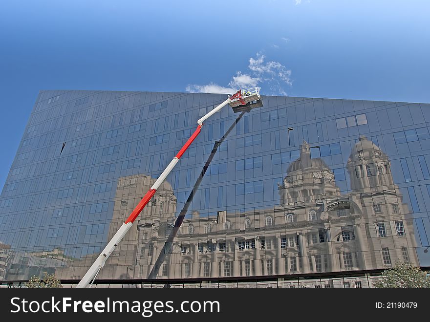 A Red and White Cherry Picker and Glass Building with Reflection of a Historic Building