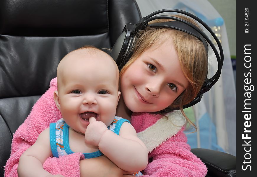 Two girls sit on a chair with headphones and listen to music. Two girls sit on a chair with headphones and listen to music