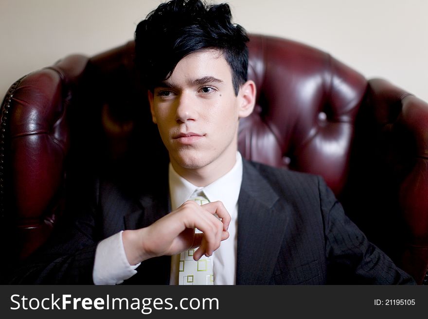 A handsome young man in a business suit, seated on a plush leather chair, looking camera left. A handsome young man in a business suit, seated on a plush leather chair, looking camera left.