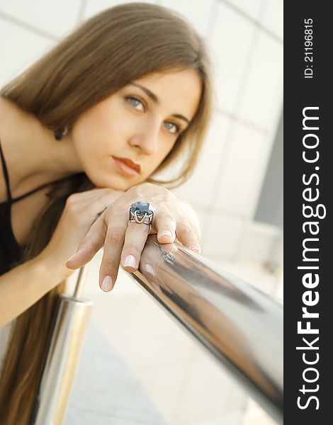 Portrait of elegantly beautiful young woman is based on the railing. The girl beautiful jewelry, ring and earrings with large blue stones