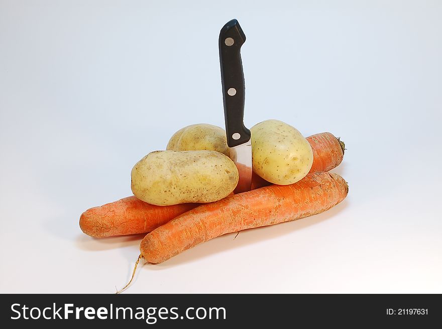 Vertically positioned knife with few carrots and potatoes. Vertically positioned knife with few carrots and potatoes