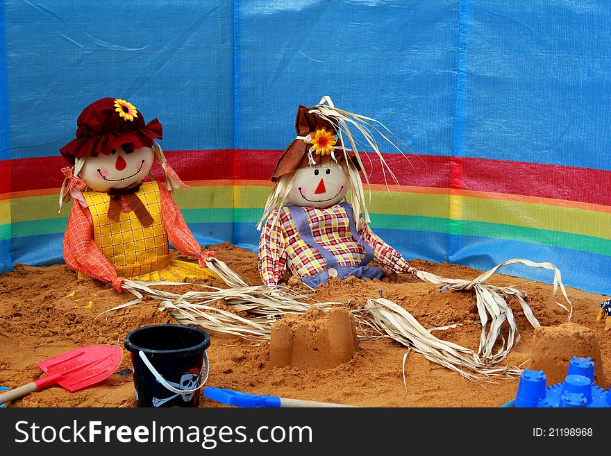 Two colourful scarecrows sitting on the sand with a wind break and buckets and spades. Two colourful scarecrows sitting on the sand with a wind break and buckets and spades