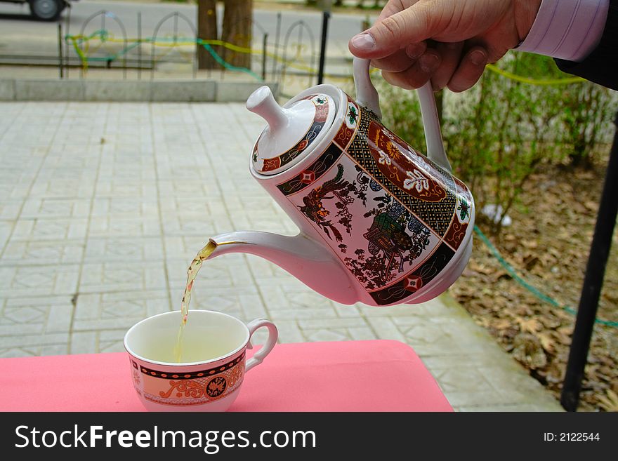 Pouring green tea in a teacup on a red table. Pouring green tea in a teacup on a red table