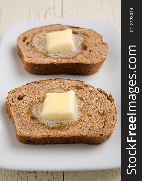 Cinnamon raisin toast with butter on a white plate. Butter melting in a pool. Cinnamon raisin toast with butter on a white plate. Butter melting in a pool.