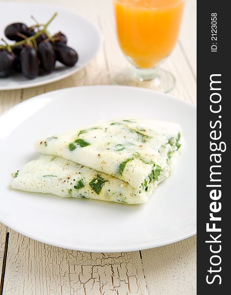 Egg white and spinach omelet with fruit on a white plate and Orange juice on the side