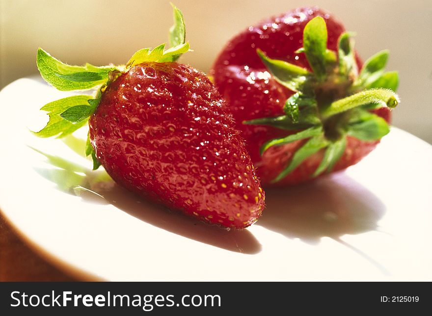 Red strawberry with green leaves on  white plate