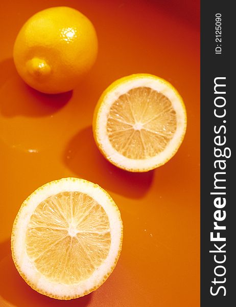 Whole yellow lemon and two slices of lemon on an orange background