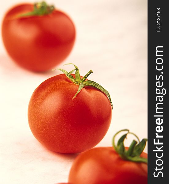 Three red tomatoes with green leaves on white background