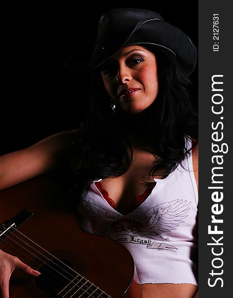 Classic country girl close up portrait wearing hat with moody shadow on her face holding guitar on black background. Classic country girl close up portrait wearing hat with moody shadow on her face holding guitar on black background