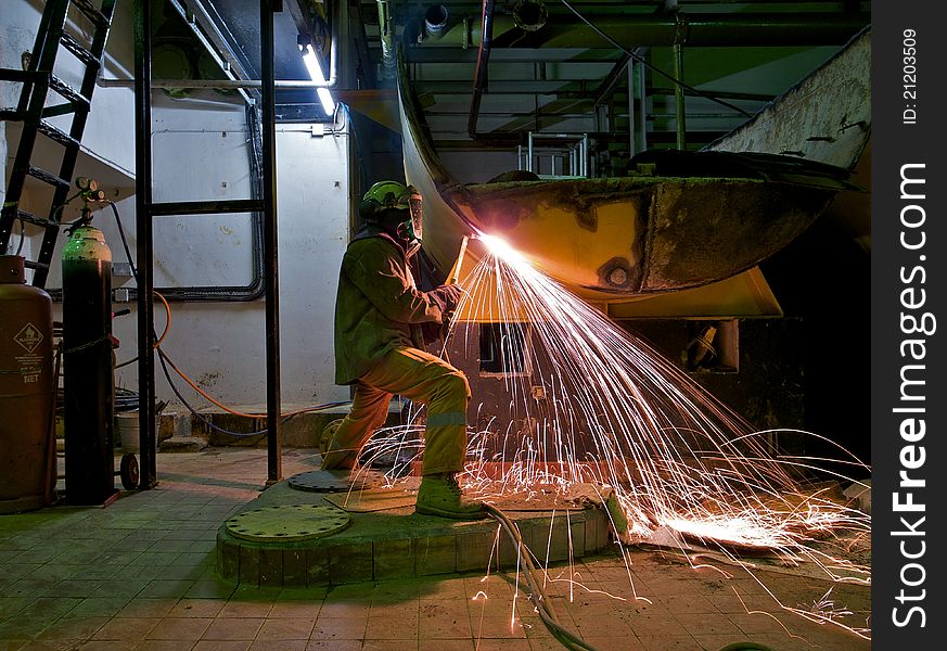 A workman flame cutting a lage metal tank. A workman flame cutting a lage metal tank