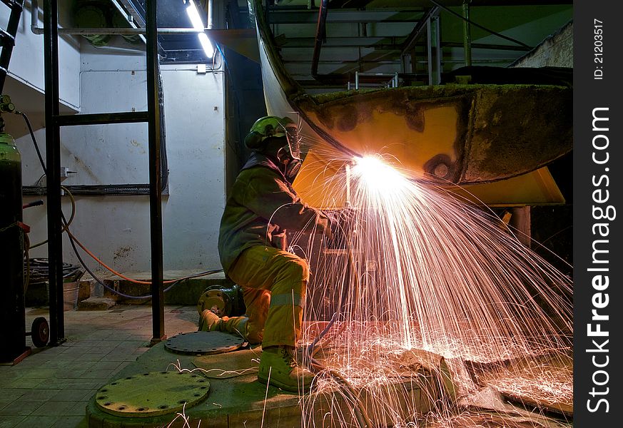 A workman flame cutting a lage metal tank. A workman flame cutting a lage metal tank