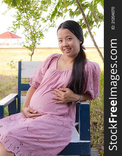 Asian pregnant woman in pink dress smiling in park. Asian pregnant woman in pink dress smiling in park