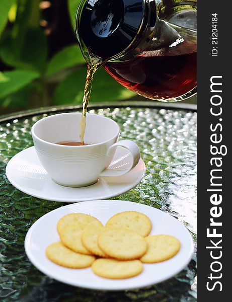 Tea poured into a cup served with lemon biscuits in warm afternoonlight outdoor. Tea poured into a cup served with lemon biscuits in warm afternoonlight outdoor