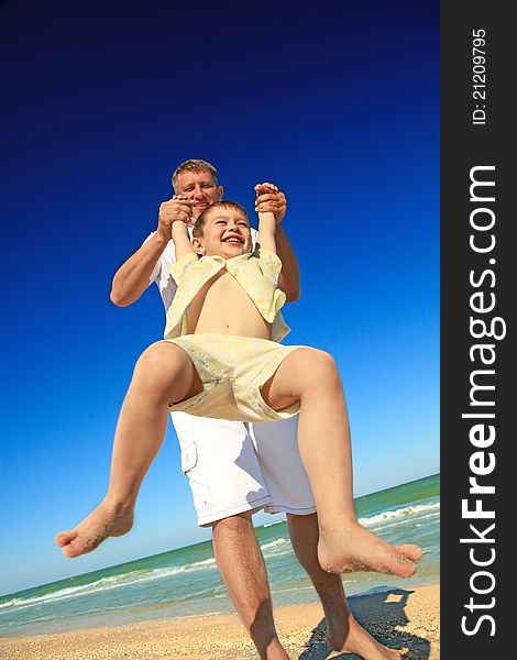 A happy boy tossed into the blue sky by his father at beach. A happy boy tossed into the blue sky by his father at beach