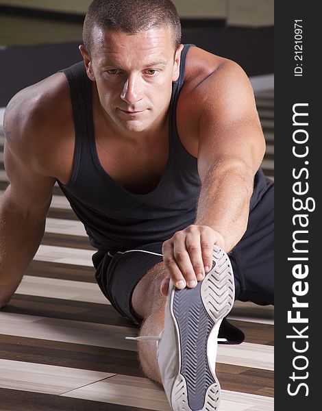 After hard workout fitness instructor is stretching his leg on the floor of the gym. After hard workout fitness instructor is stretching his leg on the floor of the gym