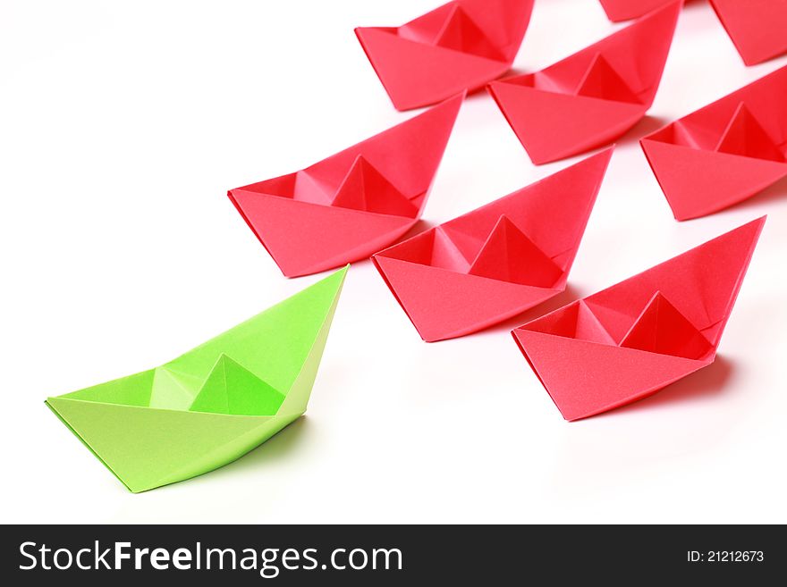 One green and several red paper boats on white background. One green and several red paper boats on white background