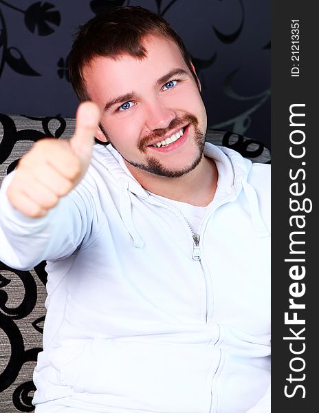 Young guy sitting on sofa and shows OK sign. Young guy sitting on sofa and shows OK sign