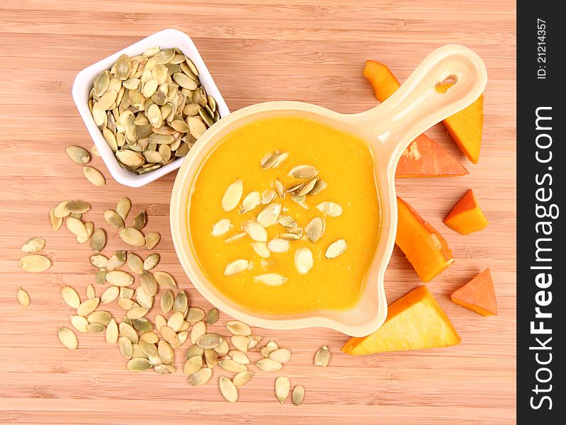Pumpkin soup, a bowl of pumpkin seeds and some pieces of pumpkin on wooden background