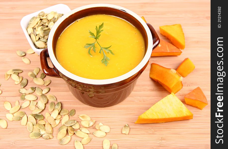 Pumpkin soup decorated with parsley, a bowl of pumpkin seeds and some pieces of pumpkin on wooden background