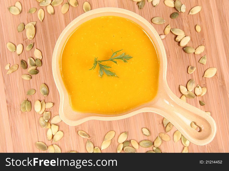 Pumpkin soup decorated with parsley and pumpkin seeds on wooden background