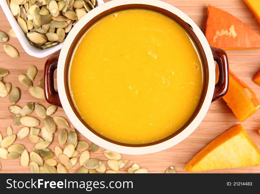 Pumpkin soup, a bowl of pumpkin seeds and some pieces of pumpkin on wooden background