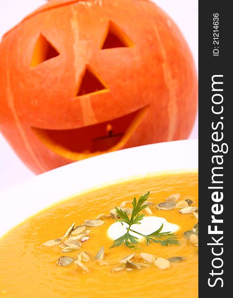 Pumpkin soup decorated with cream, pumpkin seeds and parsley with Jack-o'-lantern in the background