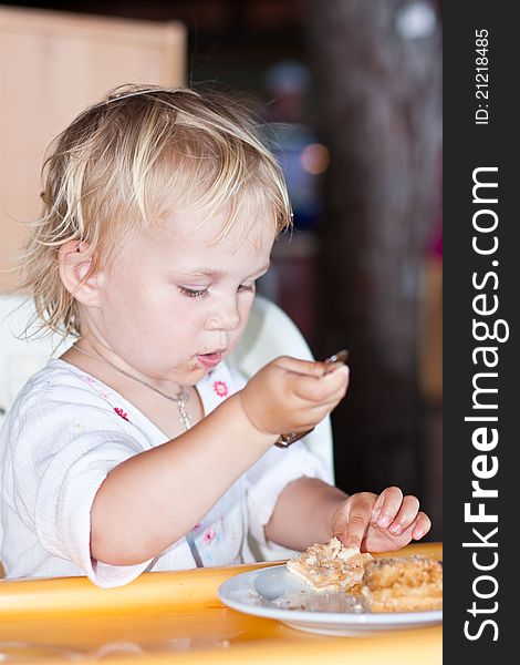 Adorable baby eating cake in a chair with a fork