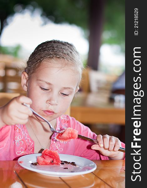 Adorable girl eating watermelon with a knife and a fork outdoor. Adorable girl eating watermelon with a knife and a fork outdoor