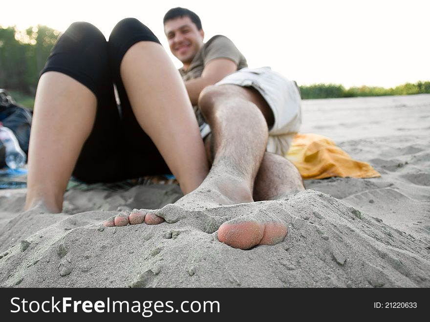 Young man with feat in sand on woman lying in the sun next to him. Young man with feat in sand on woman lying in the sun next to him